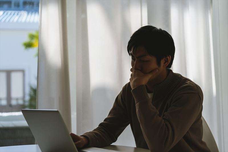 男性がパソコンの前で考え事をしている写真です